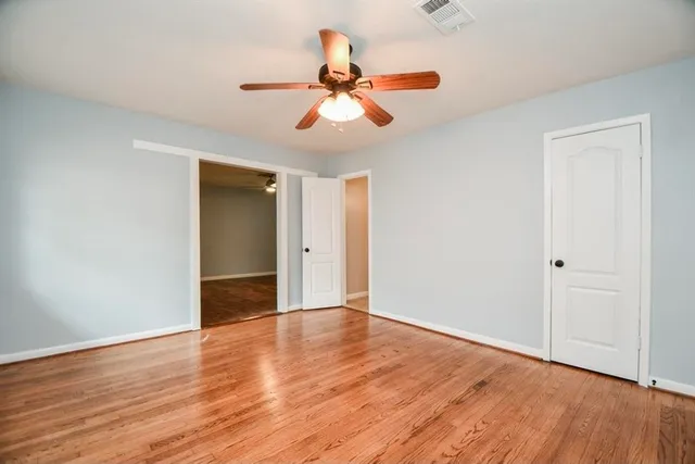 a view of an empty room with wooden floor and a ceiling fan