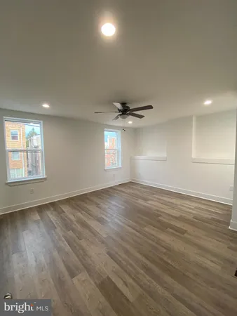an empty room with wooden floor ceiling fan and windows