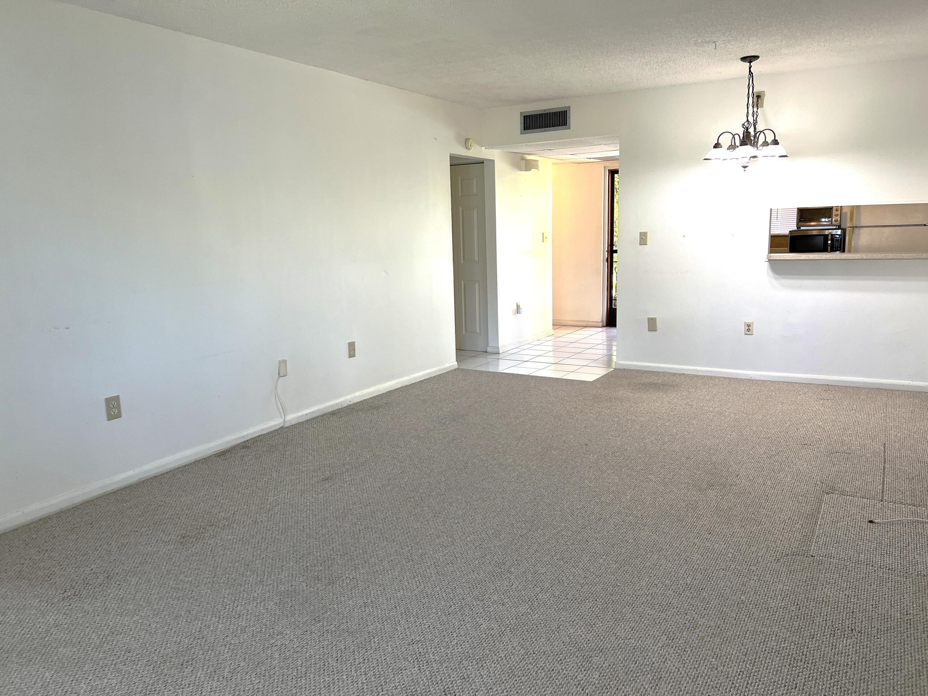 812 Southwest 9th St Circle, Unit 103 Boca Raton, FL 33486 - Photo 2 of 14 an empty room with a chandelier fan and windows