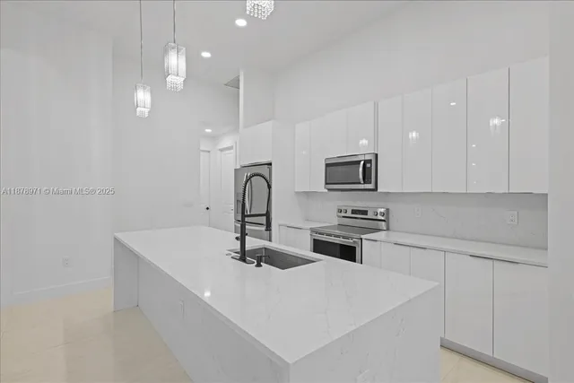 a kitchen with stainless steel appliances a sink a stove a microwave a sink a refrigerator and white cabinets