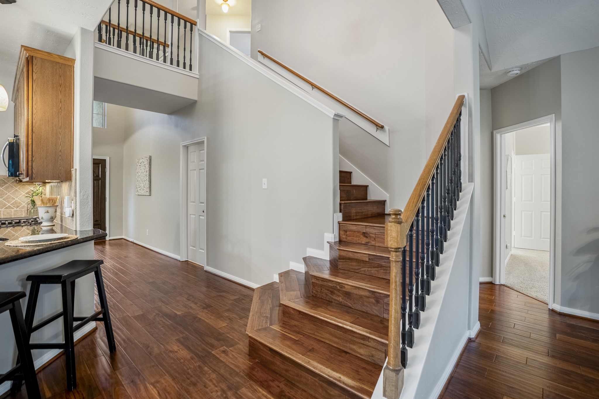 6311 Sparrows Glen Lane Spring, TX 77379 - Photo 16 of 50 This view brings the main level into focus, with the kitchen bar to one side, the front entry just beyond, and the staircase rising at the center as the home opens toward the living room and downstairs primary suite through the doorway to the right of the stairs.