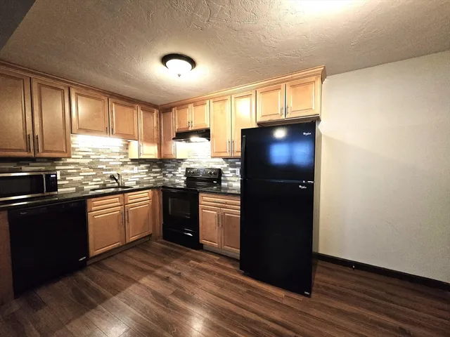 a kitchen with granite countertop stainless steel appliances a refrigerator cabinets and wooden floor