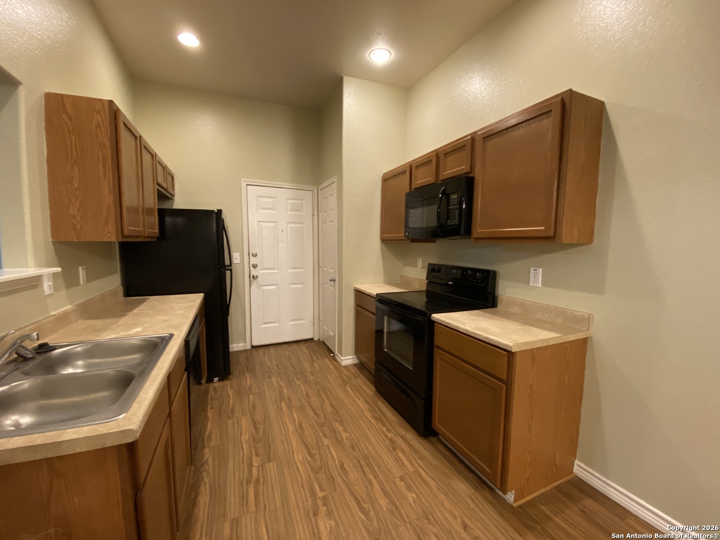 1103 Maple Street Jourdanton, TX 78026 - Photo 6 of 11 a kitchen with a sink a stove top oven and wooden floor