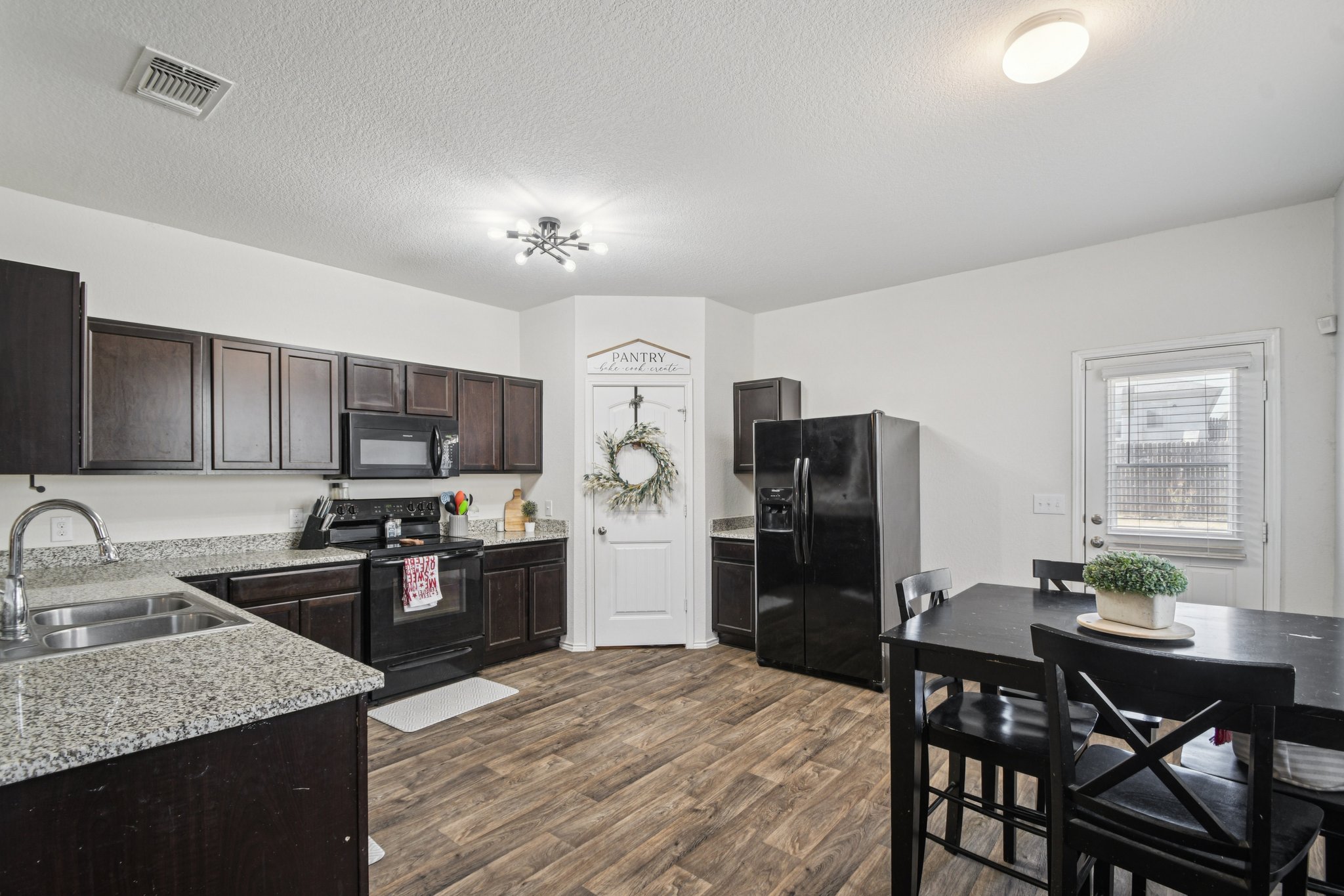 14904 Shalestone Way Manor, TX 78653 - Photo 6 of 23 Kitchen with black appliances, dark brown cabinetry, dark wood-style flooring, a textured ceiling, and light stone counters