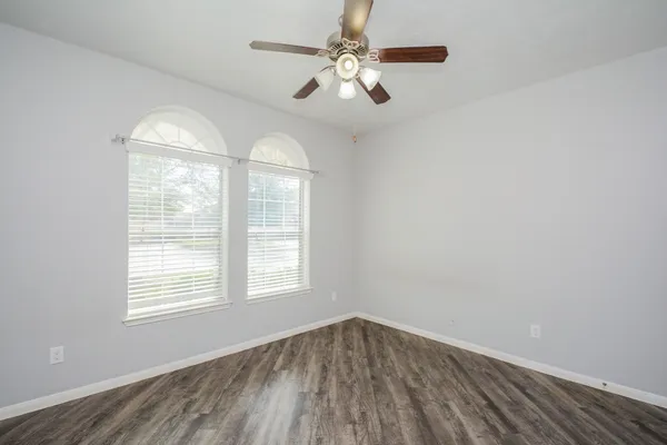 an empty room with wooden floor chandelier fan and windows