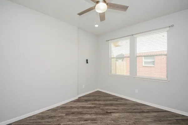 an empty room with wooden floor fan and windows