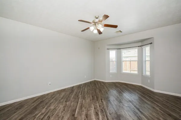 an empty room with wooden floor fan and windows