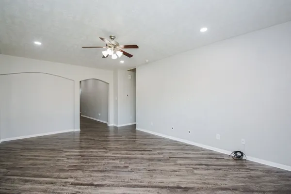 a view of an empty room with chandelier fan and wooden floor