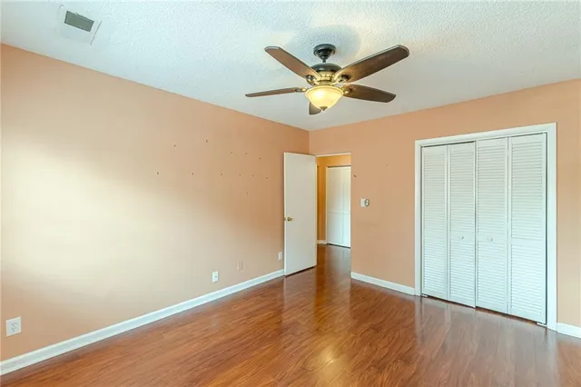 a view of an empty room with wooden floor and a ceiling fan