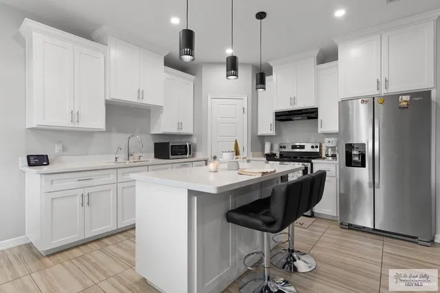 a kitchen with stainless steel appliances granite countertop a sink a stove a refrigerator and white cabinets with wooden floor