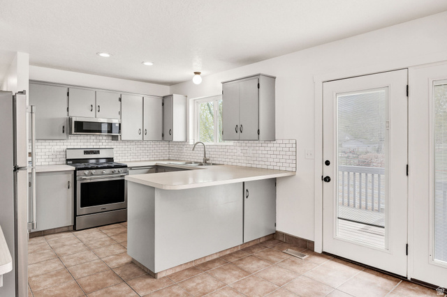 365 South Center Street Fielding, UT 84311 - Photo 12 of 41 Kitchen with a peninsula, gray cabinets, stainless steel appliances, light countertops, and decorative backsplash