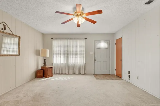 an empty room with chandelier fan and windows