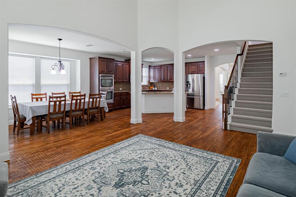 4210 Magnolia Road Melissa, TX 75454 - Photo 8 of 22 Arched doorways, wood-finish flooring, staircase with carpeted treads, dark wood cabinetry, and stainless steel appliances