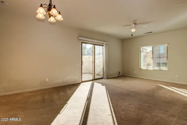 an empty room with chandelier fan and windows