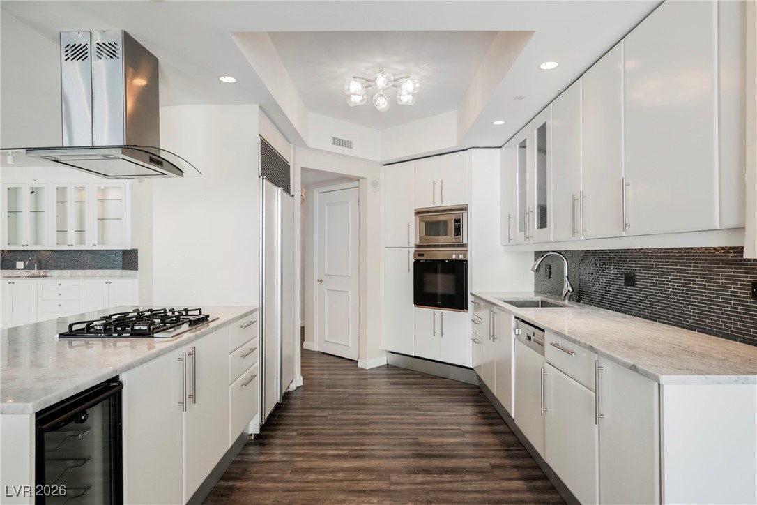 2877 Paradise Road, Unit 1604 Las Vegas, NV 89109 - Photo 12 of 47 Kitchen featuring island exhaust hood, beverage cooler, built in appliances, white cabinetry, and decorative backsplash