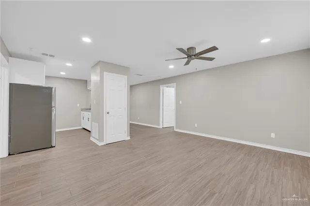a view of an empty room with wooden floor and a ceiling fan