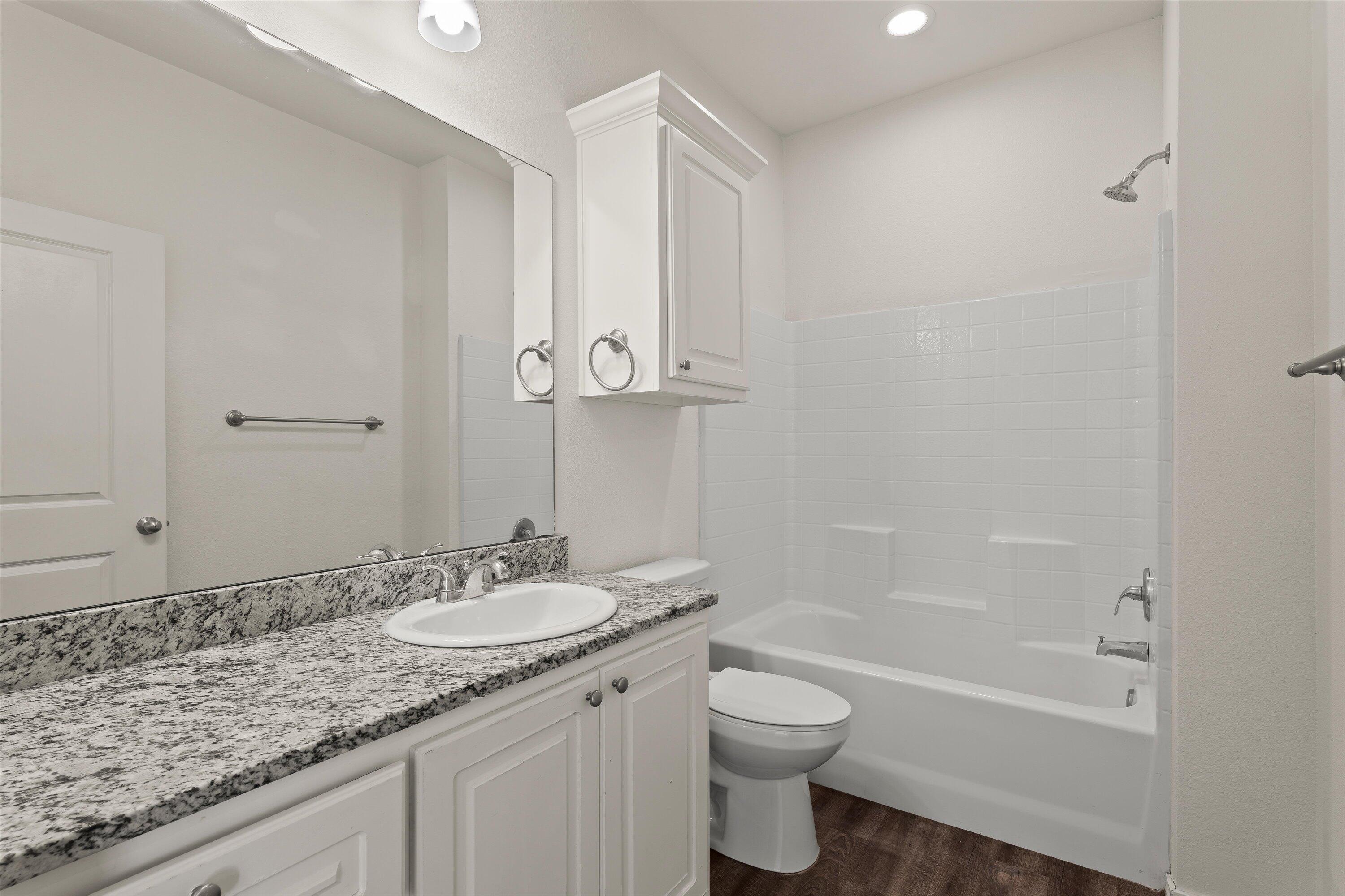 6908 21st Street Lubbock, TX 79407 - Photo 22 of 28 a bathroom with a granite countertop sink a toilet and bathtub