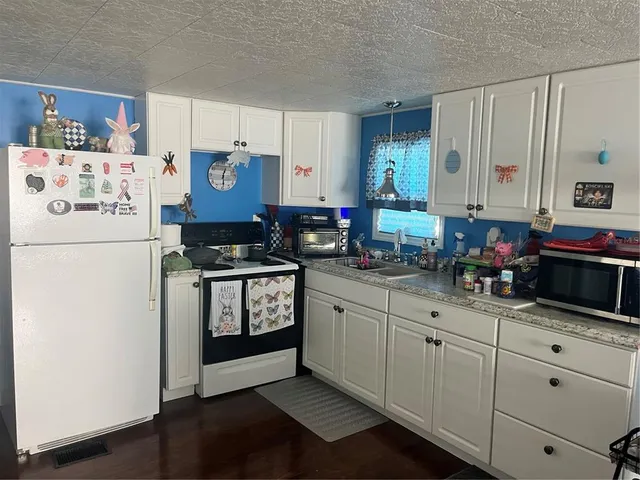 a kitchen with granite countertop a refrigerator a sink and white cabinets