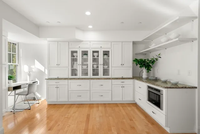 a large white kitchen with granite countertop a stove a sink a window and white cabinets