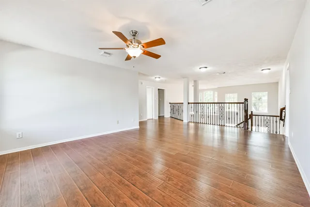 an empty room with wooden floor ceiling fan and windows