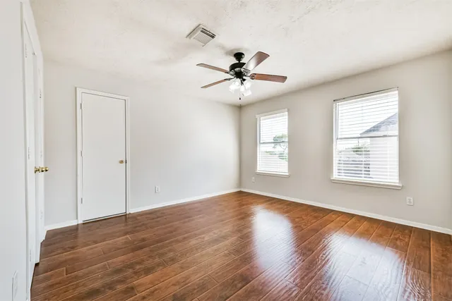 an empty room with wooden floor fan and windows