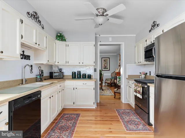 a kitchen with stainless steel appliances granite countertop a refrigerator a stove top oven a sink dishwasher and white cabinets with wooden floor