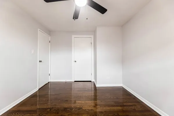 a view of an empty room with wooden floor and a ceiling fan