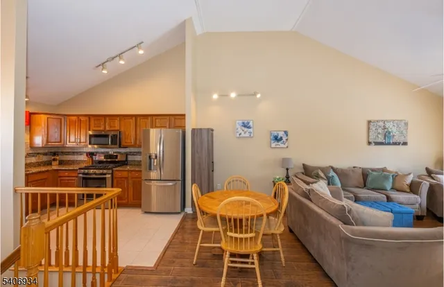 a kitchen with stainless steel appliances kitchen island granite countertop a refrigerator a stove a sink a dining table and chairs with wooden floor