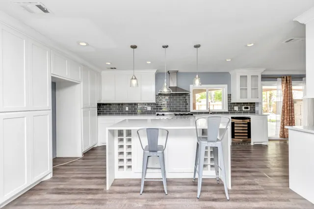 a kitchen with stainless steel appliances granite countertop a stove top oven a sink refrigerator and white cabinets with wooden floor