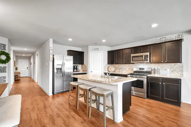 a kitchen with stainless steel appliances granite countertop a stove top oven a sink dishwasher a refrigerator and a dining table with wooden floor
