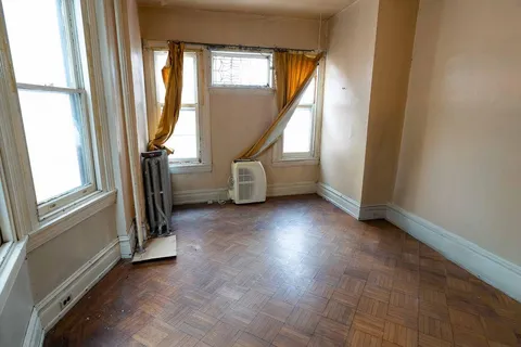 an empty room with wooden floor windows and fan