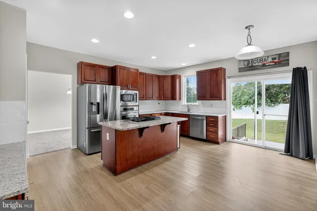 a kitchen with stainless steel appliances granite countertop a refrigerator a sink dishwasher a stove and a large countertops with wooden floor