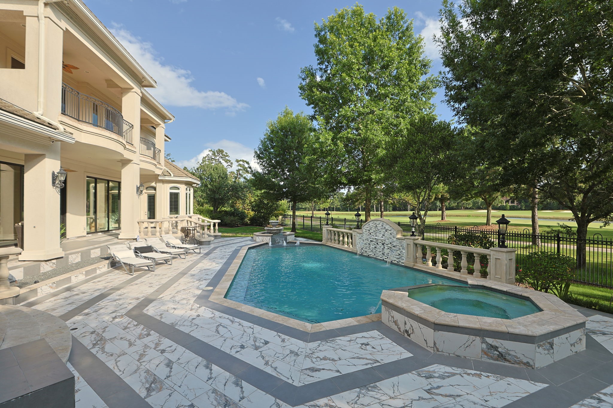 39 Maymont Way Spring, TX 77382 - Photo 39 of 50 This luxurious home features a spacious outdoor area with a beautiful pool and hot tub, surrounded by elegant stone tiling. It overlooks a lush, green landscape with mature trees, providing a serene and private setting. Perfect for relaxation and entertaining.