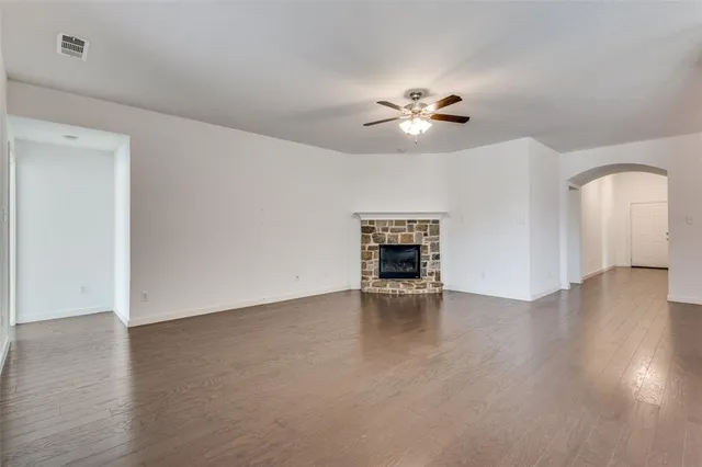 an empty room with wooden floor chandelier fan and windows