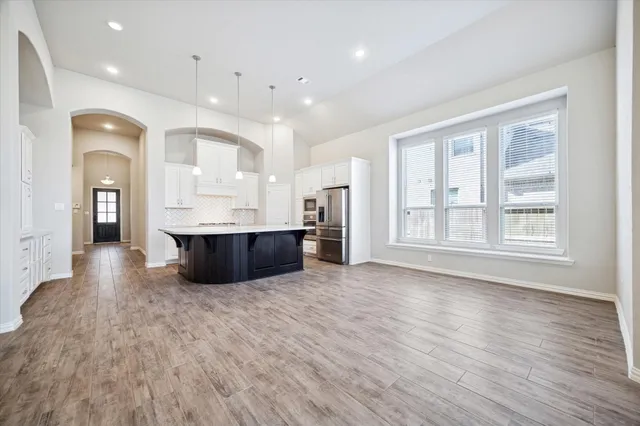 a large room with kitchen island a sink wooden floor and stainless steel appliances