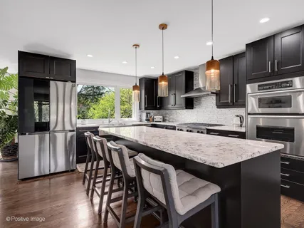 a kitchen with stainless steel appliances granite countertop a stove a refrigerator a kitchen island a sink and chairs