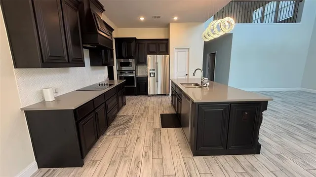 a kitchen with stainless steel appliances granite countertop wooden cabinets a refrigerator a sink and wooden floors