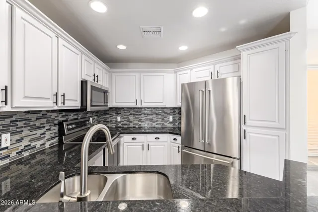 a kitchen with stainless steel appliances granite countertop a refrigerator a sink a stove and white cabinets with wooden floor