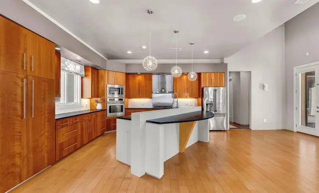 a kitchen with stainless steel appliances kitchen island granite countertop a refrigerator a sink a stove and wooden floors