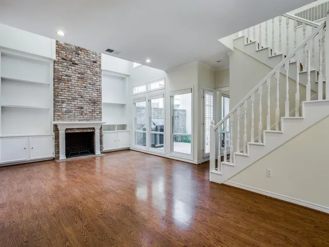 a view of an empty room with wooden floor a fireplace and a window