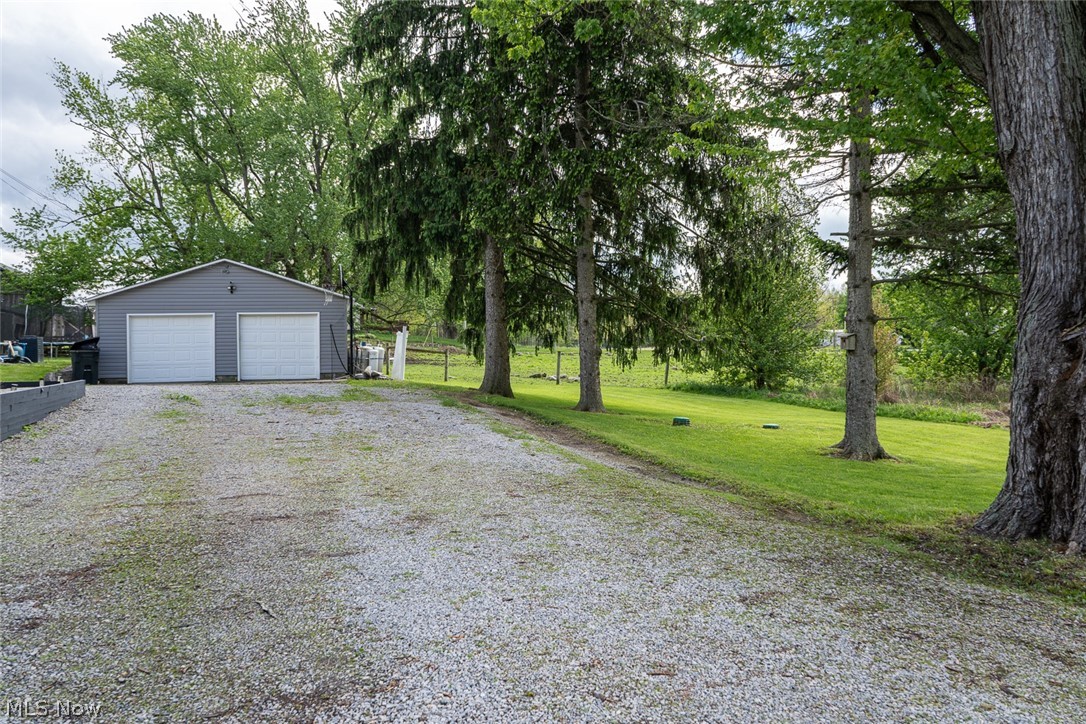 13429 West Calla Road Salem, OH 44460 - Photo 2 of 27 Two-car detached garage with white overhead doors, gravel driveway, and surrounding green lawn with mature trees