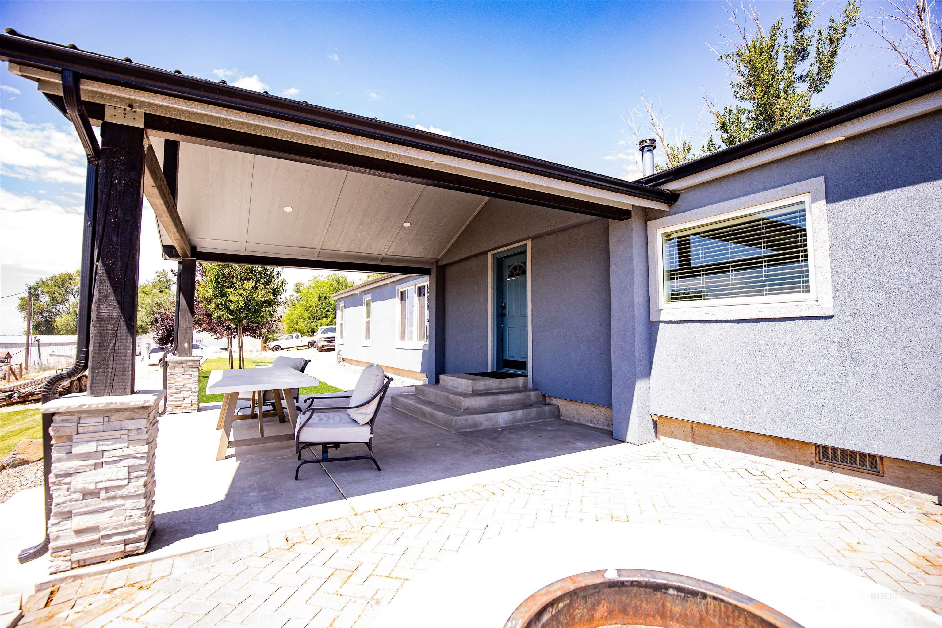 23904 Southview Lane Middleton, ID 83644 - Photo 21 of 29 Covered patio featuring stone veneer column bases, dark wood-finish posts, a light blue entry door, and a stucco exterior