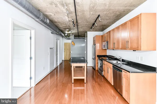 a kitchen with stainless steel appliances granite countertop a refrigerator a stove and a sink with wooden floor