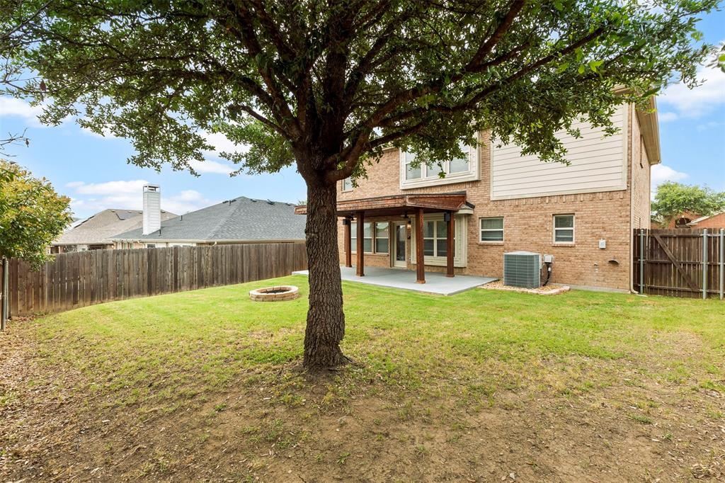 6522 Portside Ridge Lane Dallas, TX 75249 - Photo 32 of 37 Expansive backyard featuring a mature tree, stone fire pit, and a covered concrete patio with wood beams