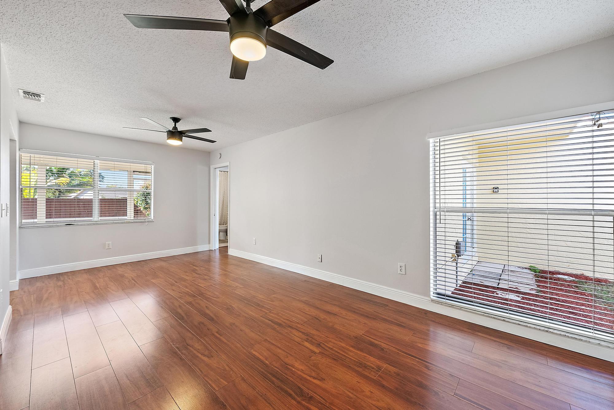 1199 Jackpine Street Wellington, FL 33414 - Photo 6 of 20 an empty room with wooden floor chandelier fan and windows