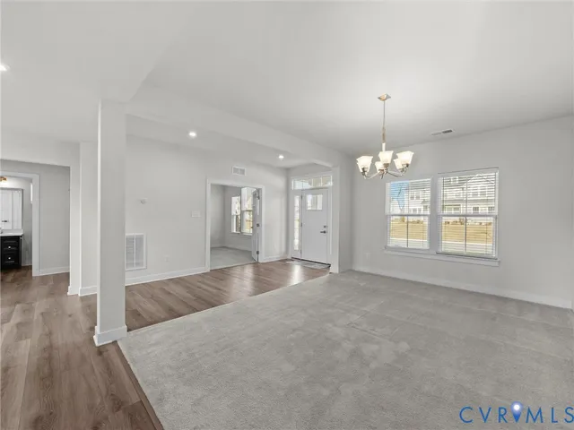 an empty room with wooden floor chandelier and windows