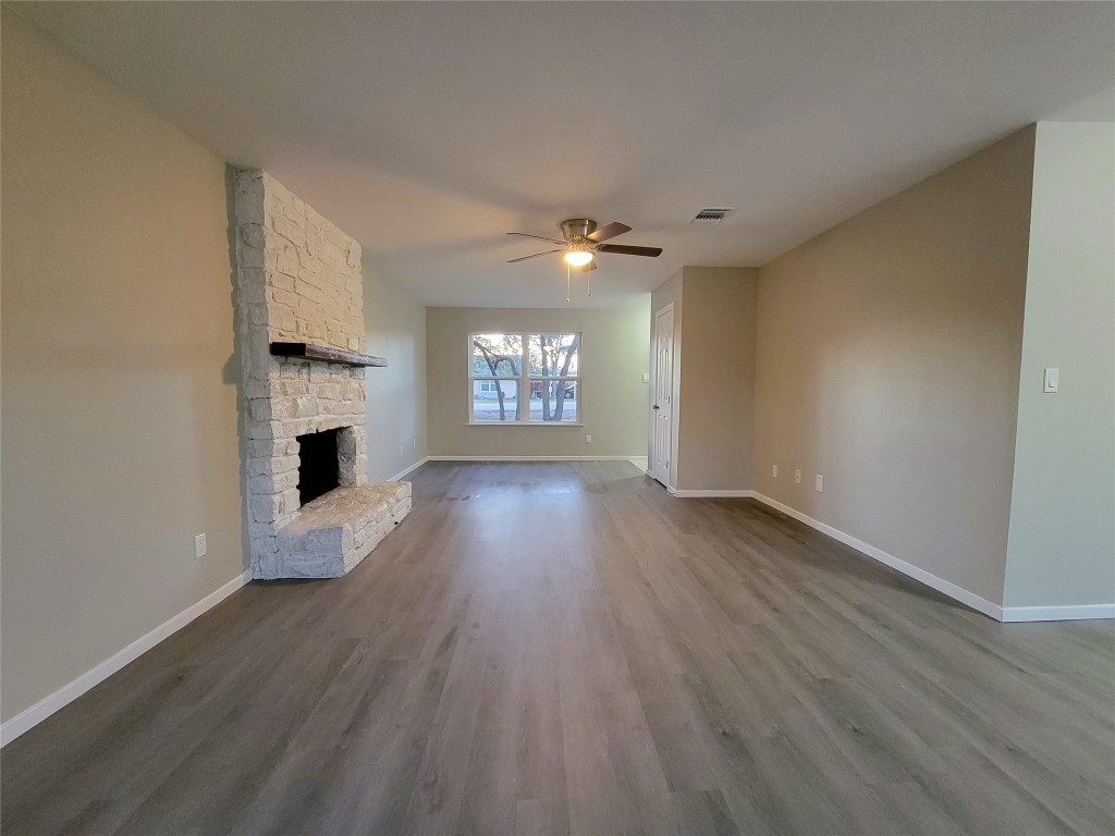 1900 Limerick Lane Leander, TX 78641 - Photo 8 of 12 Large, open, unfurnished living area with vinyl plank flooring, a stone wood burning fireplace, ceiling fan and great natural light through the new windows