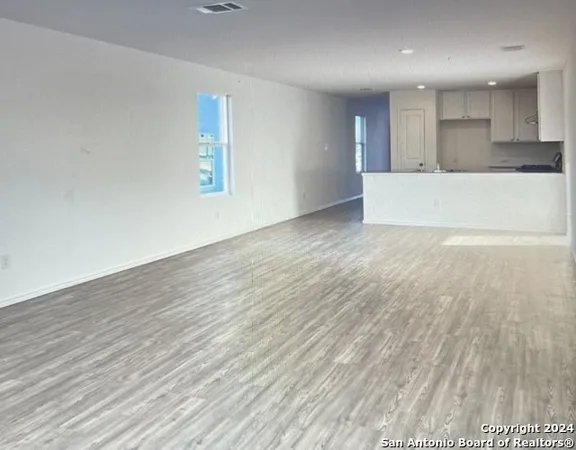 a view of an empty room with wooden floor and a kitchen