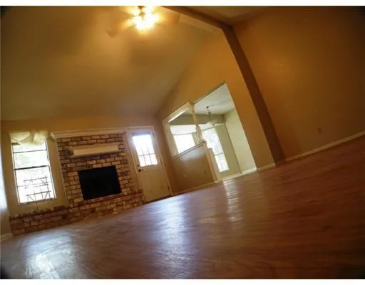 a view of an empty room with wooden floor fireplace and a window
