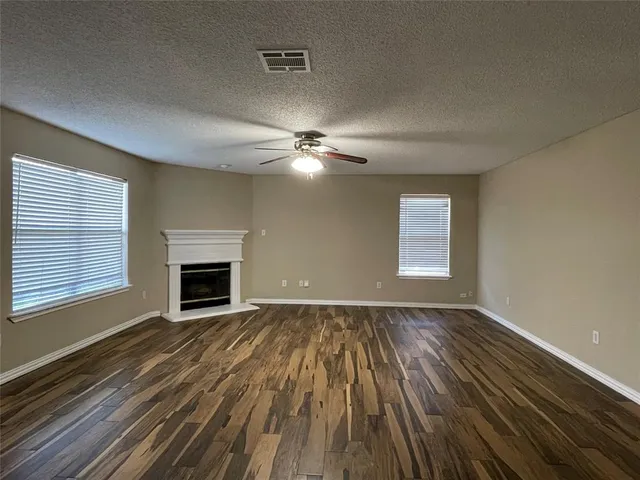 a view of an empty room with wooden floor fireplace and a window